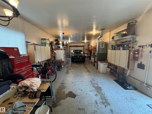 Spacious garage featuring overhead lighting, built-in cabinetry, wall-mounted shelving, a utility sink, and a window with blinds - 4502 55 Avenue, Vegreville, AB 