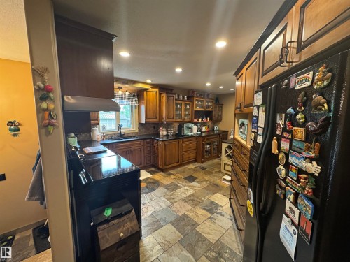 Kitchen featuring wood-finish cabinetry, dark countertops, and varied-tone tile flooring - 4502 55 Avenue, Vegreville, AB 