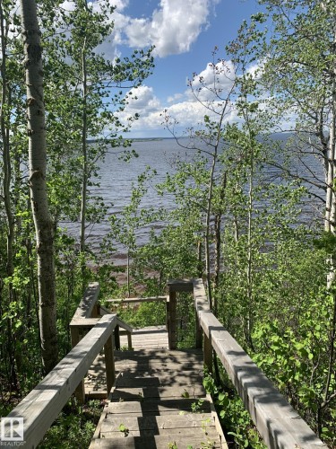 Wood-plank staircase leading to a body of water, bordered by lush trees and natural foliage - #446 67432 Mcgrane Rd, Rural Lac La Biche County, AB 