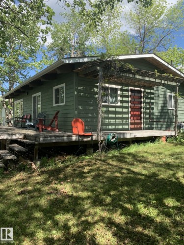 Green siding exterior featuring a wooden deck with stairs, white-trimmed windows, a red entry door, and a pergola structure - #446 67432 Mcgrane Rd, Rural Lac La Biche County, AB 