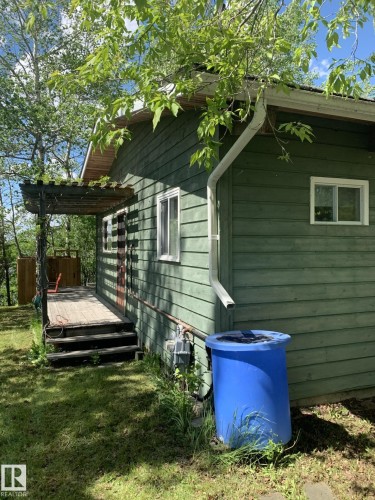 Wood-sided exterior featuring white-framed windows, a wooden deck with steps, and an overhead pergola structure - #446 67432 Mcgrane Rd, Rural Lac La Biche County, AB 