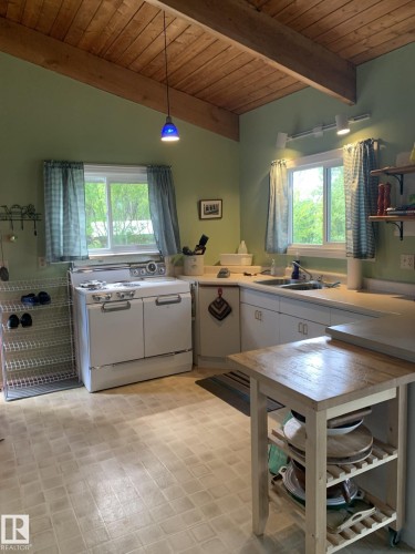 Kitchen featuring exposed wood beam ceiling, multiple windows, white cabinetry, and a white freestanding range - #446 67432 Mcgrane Rd, Rural Lac La Biche County, AB 