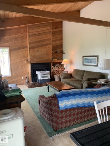 Living area featuring exposed wood ceiling beams and a striking wood-paneled accent wall with a fireplace - #446 67432 Mcgrane Rd, Rural Lac La Biche County, AB 