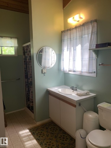 Bathroom featuring a shower stall, a single vanity with a white countertop, and a round wall mirror - #446 67432 Mcgrane Rd, Rural Lac La Biche County, AB 
