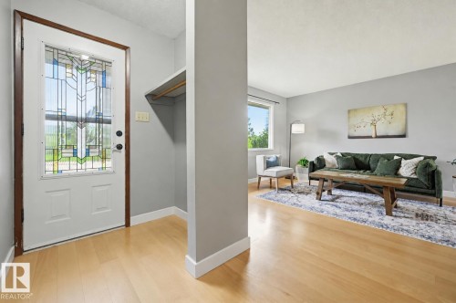Entryway featuring a white door with decorative glass, light wood-finish flooring, and a built-in coat nook - 10712 52 Avenue, Edmonton, AB 