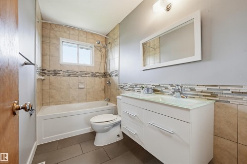 Bathroom featuring a white vanity with integrated basin, chrome fixtures, and a framed mirror - 10712 52 Avenue, Edmonton, AB 