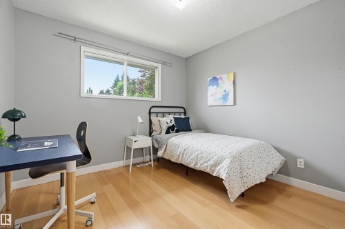 Light-filled room featuring wood-finish flooring, neutral gray walls, a white trim baseboard, and a large window providing outdoor scenery - 10712 52 Avenue, Edmonton, AB 