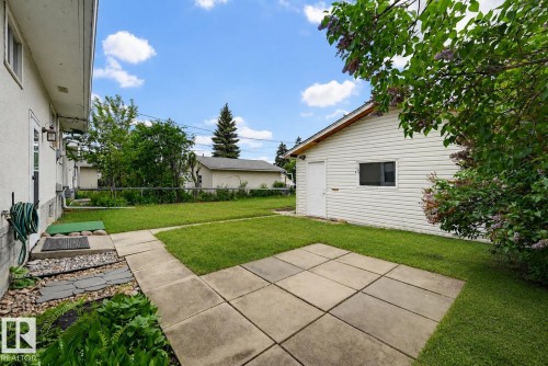 Expansive rear yard featuring a concrete patio, manicured lawn, and a detached white-sided garage with a side entry door - 10712 52 Avenue, Edmonton, AB 