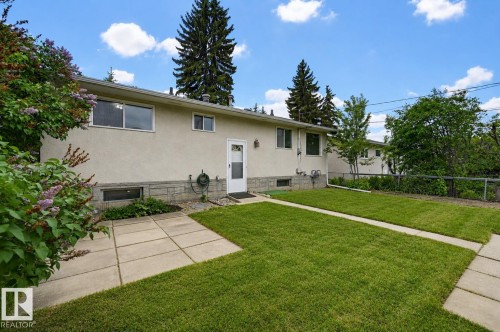 Stucco exterior featuring a stone accent band, multiple windows, and a white entry door - 10712 52 Avenue, Edmonton, AB 