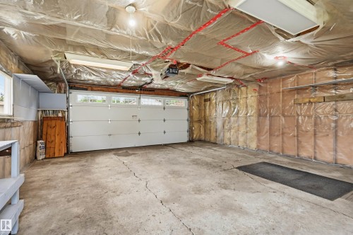 Spacious garage with a sectional garage door featuring upper window panels, exposed insulation, a concrete floor, and integrated overhead lighting - 10712 52 Avenue, Edmonton, AB 