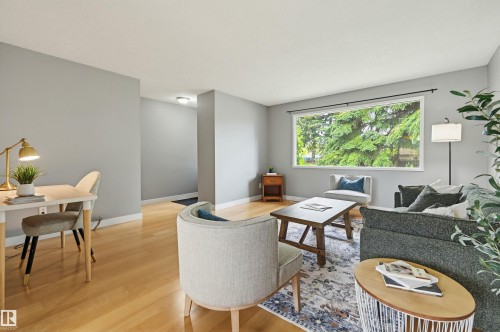 Spacious interior featuring light wood-finish flooring, a broad window overlooking mature greenery, and neutral wall tones - 10712 52 Avenue, Edmonton, AB 