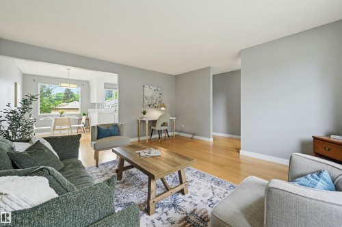 Bright living area featuring wood-finish flooring, a neutral color palette, and an open entryway to an additional room with a dining area and a large window - 10712 52 Avenue, Edmonton, AB 