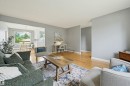 Bright living area featuring wood-finish flooring, a neutral color palette, and an open entryway to an additional room with a dining area and a large window - 10712 52 Avenue, Edmonton, AB 