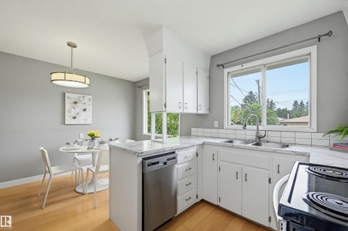 Kitchen featuring white cabinetry, light-colored countertops, stainless steel dishwasher, and a double-basin sink - 10712 52 Avenue, Edmonton, AB 