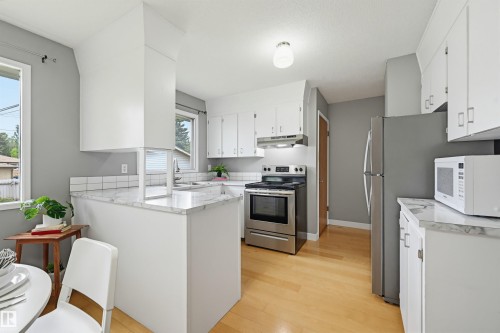 Kitchen featuring white cabinetry, wood-finish flooring, stainless steel appliances, marble-look countertops, and a white subway tile backsplash - 10712 52 Avenue, Edmonton, AB 