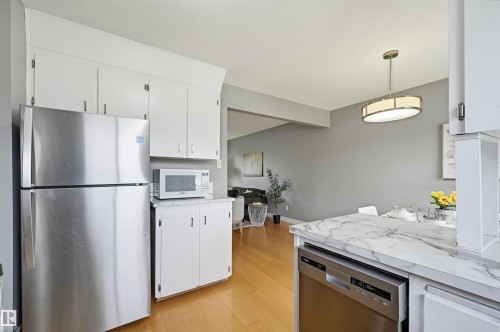 Kitchen featuring white cabinetry, stainless steel refrigerator, and integrated dishwasher - 10712 52 Avenue, Edmonton, AB 