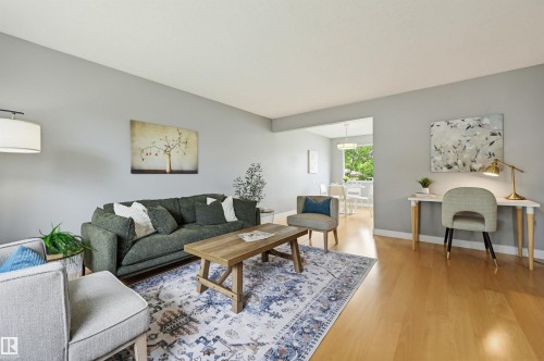 Spacious living area featuring light wood-finish flooring, neutral wall tones, and an open doorway to an additional room - 10712 52 Avenue, Edmonton, AB 