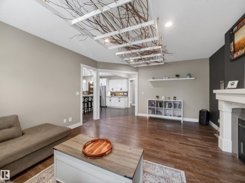 Spacious living area featuring wood-finish flooring, a decorative ceiling treatment, and a white mantel fireplace - 5608 Soleil Boulevard, Beaumont, AB 