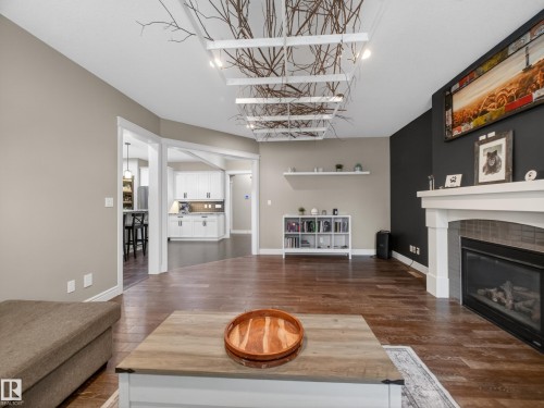 Spacious living area featuring wood-finish flooring, a white mantel fireplace with tile surround, and a unique ceiling fixture - 5608 Soleil Boulevard, Beaumont, AB 