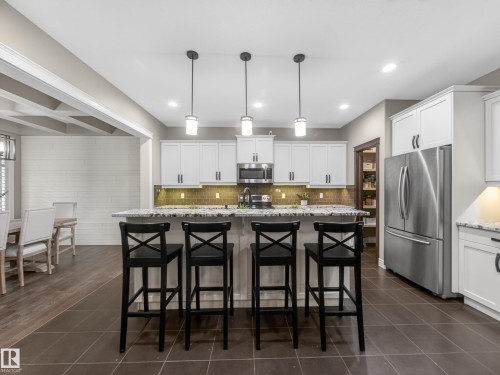 Kitchen with white cabinetry, stainless steel appliances, granite countertops, and a tiled backsplash - 5608 Soleil Boulevard, Beaumont, AB 