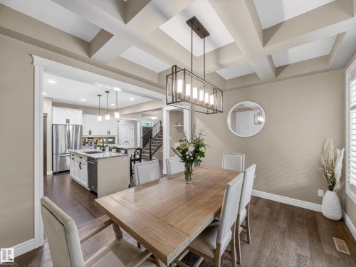 Dining area featuring a coffered ceiling, a linear chandelier, wood-finish flooring, and an archway opening to the kitchen - 5608 Soleil Boulevard, Beaumont, AB 