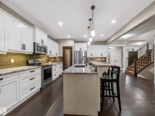 Open-concept kitchen featuring white shaker cabinetry, granite countertops, and a subway tile backsplash - 5608 Soleil Boulevard, Beaumont, AB 