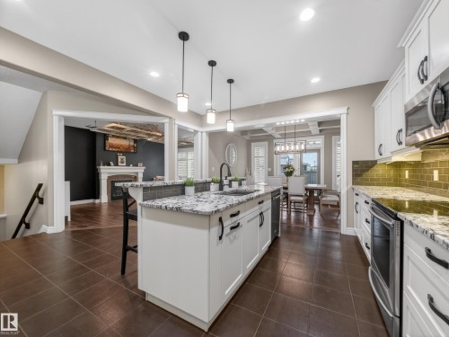 Modern kitchen featuring a central island with undermount sink, granite countertops, white cabinetry, and stainless steel appliances - 5608 Soleil Boulevard, Beaumont, AB 