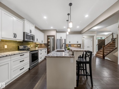 Gourmet kitchen featuring white shaker cabinetry, stainless steel appliances, granite countertops, a tiled backsplash, and a central island with pendant lighting - 5608 Soleil Boulevard, Beaumont, AB 