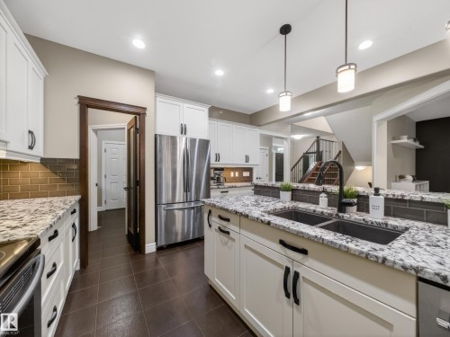 Well-appointed kitchen featuring white cabinetry, stainless steel appliances, speckled countertops, and a subway tile backsplash - 5608 Soleil Boulevard, Beaumont, AB 