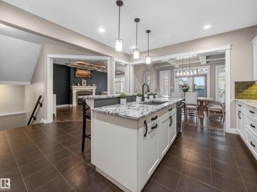Kitchen featuring a large central island with a built-in sink and pendant lighting, white cabinetry, granite countertops, and a green tile backsplash - 5608 Soleil Boulevard, Beaumont, AB 