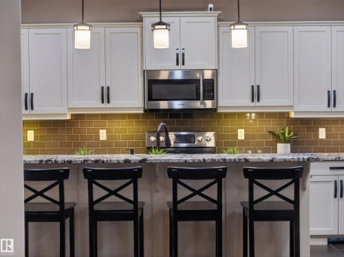 Kitchen featuring white shaker cabinetry, stainless steel microwave, stone-finish countertops, and a subway tile backsplash - 5608 Soleil Boulevard, Beaumont, AB 