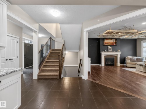 Open interior featuring a carpeted staircase with wood and metal railings, brown tile flooring, and a formal entryway - 5608 Soleil Boulevard, Beaumont, AB 