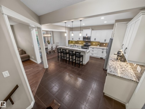Spacious kitchen featuring an island with seating, pendant lighting, stainless steel appliances, granite countertops, and tile flooring - 5608 Soleil Boulevard, Beaumont, AB 