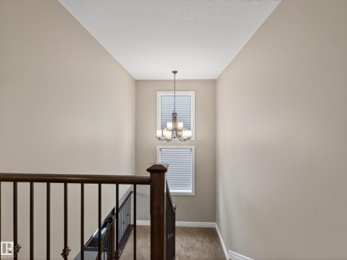 Stairwell landing featuring a decorative chandelier, two vertically stacked windows with blinds, a dark wood-finish handrail, and wrought iron balusters - 5608 Soleil Boulevard, Beaumont, AB 
