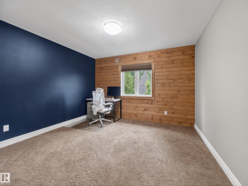 Room featuring a textured accent wall, wood-finish paneling, and soft carpet flooring - 5608 Soleil Boulevard, Beaumont, AB 
