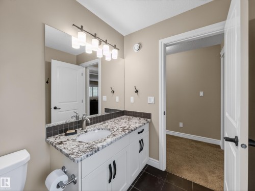 Bathroom vanity featuring white cabinetry with dark hardware, a light-colored stone countertop with an integrated sink, and a dark tile backsplash - 5608 Soleil Boulevard, Beaumont, AB 
