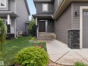 Front exterior featuring a dark wood-finish entry door, stone-clad porch columns, concrete steps, and gray horizontal siding - 5608 Soleil Boulevard, Beaumont, AB 