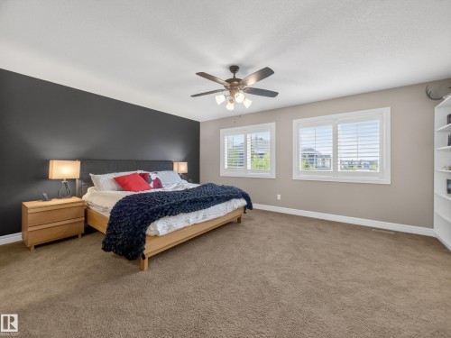 Carpeted room featuring a dark accent wall, two windows with white plantation shutters, a ceiling fan with integrated lighting, and built-in shelving - 5608 Soleil Boulevard, Beaumont, AB 