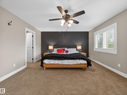 Carpeted room featuring a dark accent wall, a ceiling fan with integrated lighting, a window with white louvered shutters, and a paneled interior door - 5608 Soleil Boulevard, Beaumont, AB 