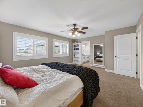 Carpeted room featuring two windows with white plantation shutters, a ceiling fan with integrated lighting, and a built-in shelving unit - 5608 Soleil Boulevard, Beaumont, AB 