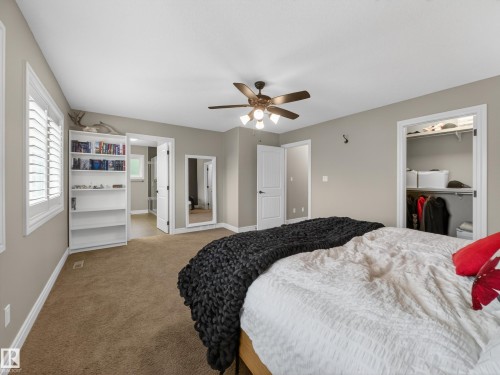 Carpeted room featuring a ceiling fan, built-in shelving, two windows with plantation shutters, and two doorways - 5608 Soleil Boulevard, Beaumont, AB 