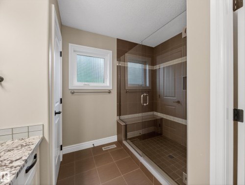 Walk-in shower featuring glass enclosure, tiled walls with accent stripe, integrated bench, and a window - 5608 Soleil Boulevard, Beaumont, AB 