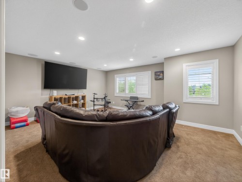 Spacious entertainment room featuring recessed lighting, multiple windows with white plantation shutters, and a wall-mounted television - 5608 Soleil Boulevard, Beaumont, AB 