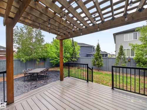 Expansive outdoor living area featuring a wood pergola with string lighting, composite decking, and black metal railings - 5608 Soleil Boulevard, Beaumont, AB 