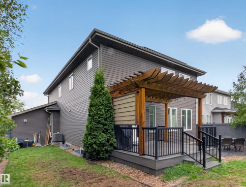 Rear exterior featuring a spacious deck with a wood pergola, dark composite decking, and black metal railings - 5608 Soleil Boulevard, Beaumont, AB 