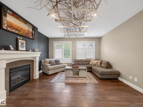 Living area featuring wood-finish flooring, a contemporary fireplace with a white mantel and brick surround, and multiple windows with plantation shutters - 5608 Soleil Boulevard, Beaumont, AB 