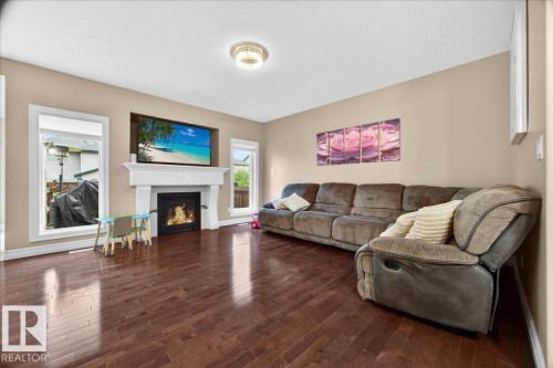 Living area featuring rich wood-finish flooring, a built-in fireplace with a white mantel, and recessed media niche - 1326 Cunningham Drive, Edmonton, AB 
