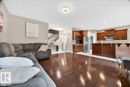 Open-concept living area featuring rich wood-finish flooring, a kitchen with wood cabinetry, stainless steel appliances, and a breakfast bar - 1326 Cunningham Drive, Edmonton, AB 