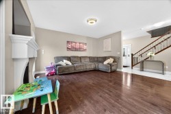 Spacious living area featuring rich wood-finish flooring and a white decorative fireplace mantel - 