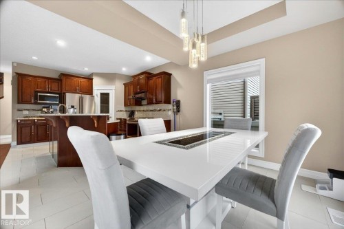 Modern dining area featuring a white rectangular table with a central inset, complemented by contemporary pendant lighting - 1326 Cunningham Drive, Edmonton, AB 